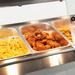 Buffet with three metal trays containing fried chicken, pasta, and other food items.