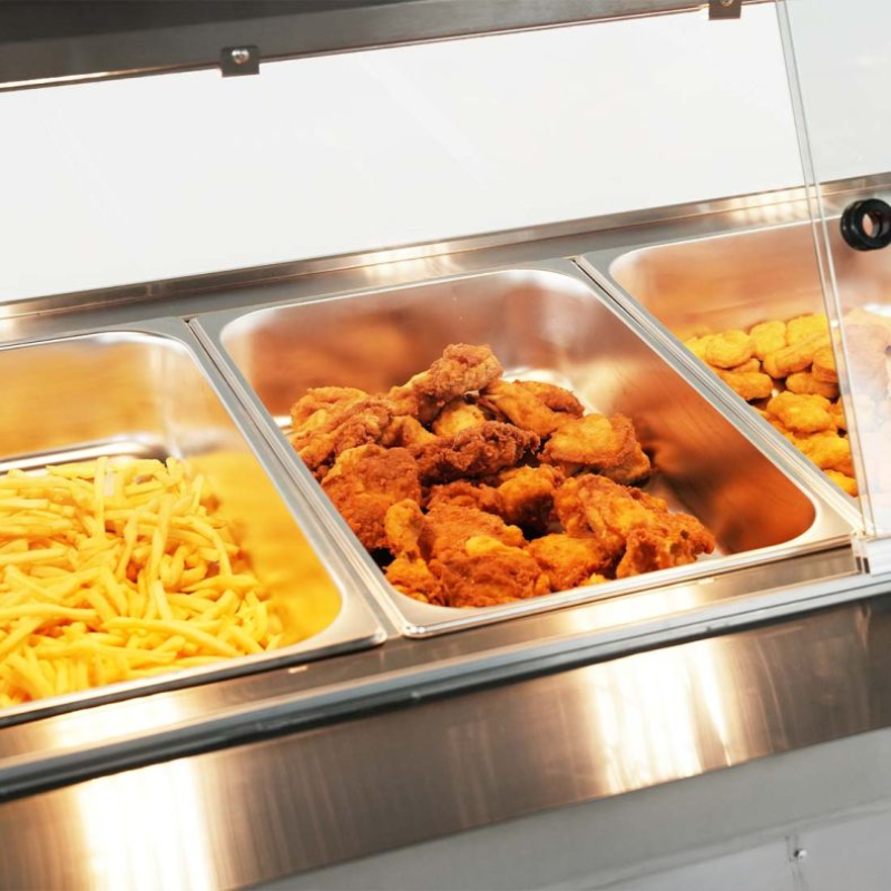 Buffet with three metal trays containing fried chicken, pasta, and other food items.
